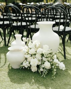 white flowers and vases are on the grass near black chairs at an outdoor ceremony