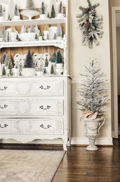 a white christmas tree sitting on top of a wooden table next to a tall white china cabinet