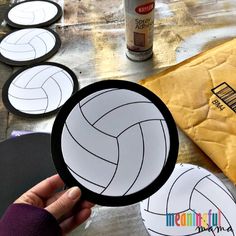 a person holding up a paper plate with volleyballs on it and other items around the table