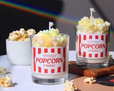 two glasses filled with popcorn sitting on top of a table next to a bowl of popcorn