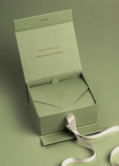 an open green box with a white ribbon on the side and a card in it