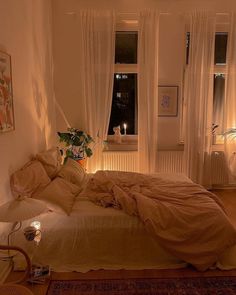 an unmade bed in a white room with candles on the windowsill and curtains