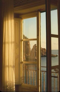 an open window looking out at the ocean and rocks in the distance from a room with sheer curtains