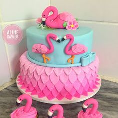 a blue and pink cake with flamingos sitting on it's sides, surrounded by other decorations