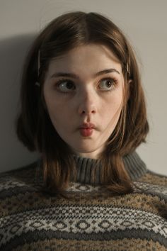 a young woman with brown hair and blue eyes wearing a sweater looking at the camera