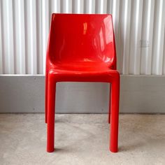 a red plastic chair sitting in front of a white wall