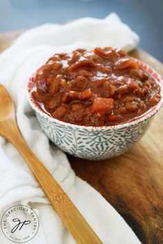 a bowl filled with chili on top of a wooden cutting board next to a spoon