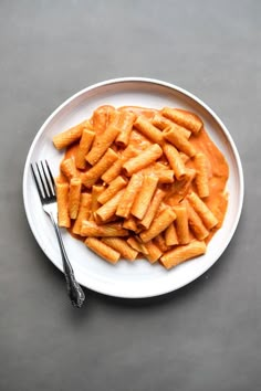 a white plate topped with pasta and sauce next to a fork on top of a table