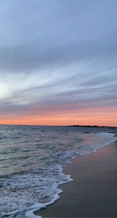 an ocean beach with waves coming in to shore and the sun setting on the horizon