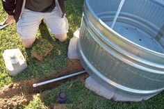 a man kneeling down next to a metal barrel with holes in the ground near it