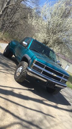 a large blue truck parked on the side of a dirt road next to trees and bushes