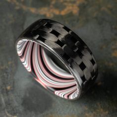 "TheCarbonForge #025 The 3k Twill Carbon Fiber Ring lined with Tilted Fordite. It's sleek, it's stylish, and it's finished with a glasslike gloss that's sure to get compliments. -Carbon Fiber Weaves- At TheCarbonForge, I take pride in offering the highest quality carbon fiber rings available. Unlike other carbon fiber rings that are simply cut from a block and shaped into a ring, my process has been specifically engineered for ring making, and produces much less waste. By tightly rolling the carbon fiber onto precision cut mandrels and curing them in an autoclave, I ensure the strongest and most durable carbon fiber rings on the market. This means that your ring will not only be beautiful, but also built to last. One of the biggest advantages of my rings is the availability of many beautif Fiber Rings, Carbon Fiber Ring, Carbon Fiber Rings, Ring Making, Black Ring, How To Make Rings, Ring Displays, Precision Cut, Mens Wedding Bands