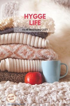 a stack of sweaters and an apple on top of a blanket with the words hygge life it's all about being cozy