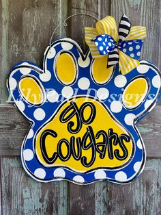 a blue and yellow dog paw shaped door hanger with the words go cougas on it