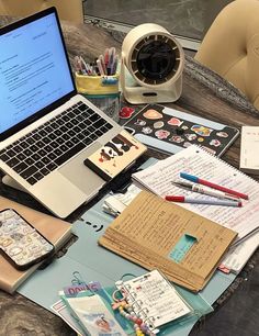 an open laptop computer sitting on top of a table covered in papers and other items