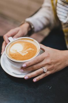 a woman holding a cup of coffee on top of a white saucer in her hands