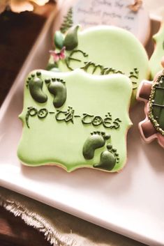 two decorated cookies sitting on top of a white plate with green icing and writing