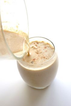 a pitcher pouring milk into a glass filled with liquid on top of a white table