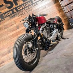 a red motorcycle parked in front of a wooden wall with the words shop & custom bikes on it