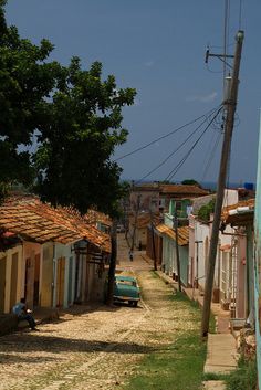 an old car parked on the side of a dirt road next to buildings and trees