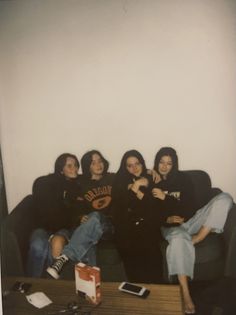 four women sitting on a couch in front of a coffee table with a cell phone