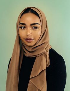 a woman wearing a brown hijab and looking at the camera with an intense look on her face