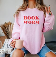 "Bookworm Sweatshirt With a super-soft fleecy interior, this sweatshirt is sure to provide absolute comfort whilst looking good! Perfect to treat yourself or gift to an avid reader! This stand-out sweater reads, 'book worm', in a bold red font. Unisex fit baby pink sweatshirt printed with permanent red vinyl. Note ~ Please double check the size before you order ~ SIZE GUIDE ~ XS - 34\" S - 36\" M - 40\" L - 44\" XL - 48\" 2XL - 52\" 3XL - 56\" ~ CARE INSTRUCTIONS ~ *Machine wash at 30o. *Tumble dry on low heat. *Iron inside-out on low setting. *Do not dry clean. *Do not bleach.  ~T-SHIRT DETAILS ~ *Unisex fit. *80% ringspun cotton, 20% polyester jumper. *280gsm weight. *Printed with high-quality permanent red vinyl. Please note - I have tried to represent the colours to the best of my abil Bookworm Sweatshirt, Writer Aesthetic, Bleach T Shirt, Slogan Sweater, Baby Pink Sweater, Cosy Jumper, Red Vinyl, Avid Reader, Book Worm