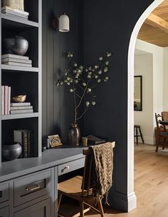 a room with black walls and wooden flooring is decorated with bookshelves, vases and flowers