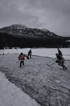 several people playing hockey in the snow with mountains in the backgrouds behind them