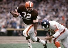 a football player running with the ball in his hand and another person behind him holding an orange and white football