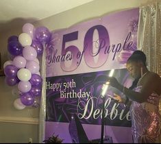 a woman standing in front of a sign that reads 50 years of purple with balloons