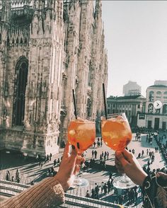 two people holding up glasses with drinks in front of an old building and the cathedral