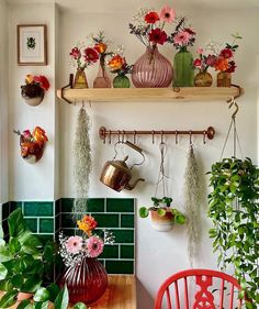 some plants and flowers are hanging on the wall above a table with two red chairs