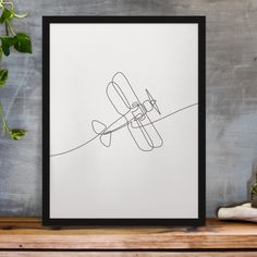 a drawing of an airplane on a white paper with black frame next to a plant