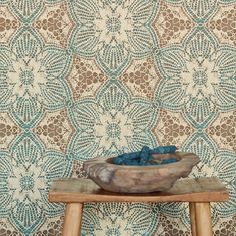 a bowl on a stool in front of a wallpapered background with an intricate design