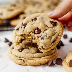 a hand picking up a chocolate chip cookie from the pile on top of other cookies