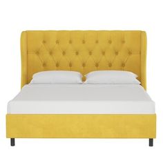 an upholstered bed with white sheets and yellow headboard