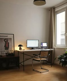 there is a desk with two computers on it and a plant in front of the window