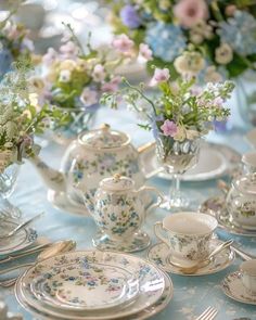 a table topped with lots of white and blue dishes covered in floral designs next to vases filled with flowers