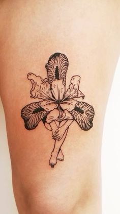 a cross tattoo on the side of a woman's thigh, with leaves and flowers