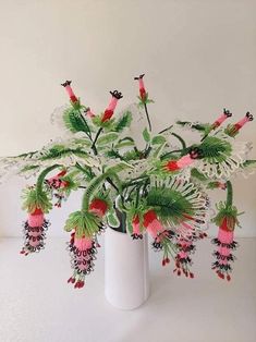 a white vase filled with lots of green and red flowers on top of a table