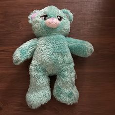 a green teddy bear sitting on top of a wooden floor next to a brown wall