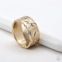 a gold wedding ring with an engraved design on the front and center, sitting on a white surface