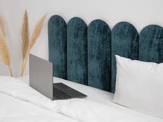 an open laptop computer sitting on top of a bed next to pillows and headboard