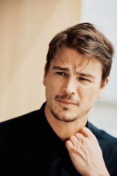 a man with his hand on his chin looking at the camera while wearing a black shirt