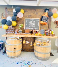 a wooden table topped with two barrels filled with drinks and balloons next to a sign