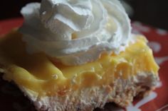 a piece of cheesecake with whipped cream on top is sitting on a red and white plate