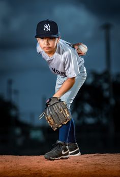 a young boy in a baseball uniform holding a ball and mitt on the field