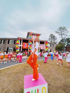 a woman standing on top of a pink block in front of a building with lots of people