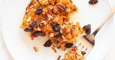 a white plate topped with fruit and nuts next to a fork on top of a table